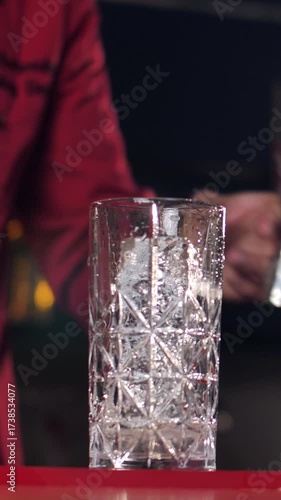 A real professional bartender creating a cocktail. Experienced bartender pouring an alcoholic drink into a glass before serving - close-up food and drink concept