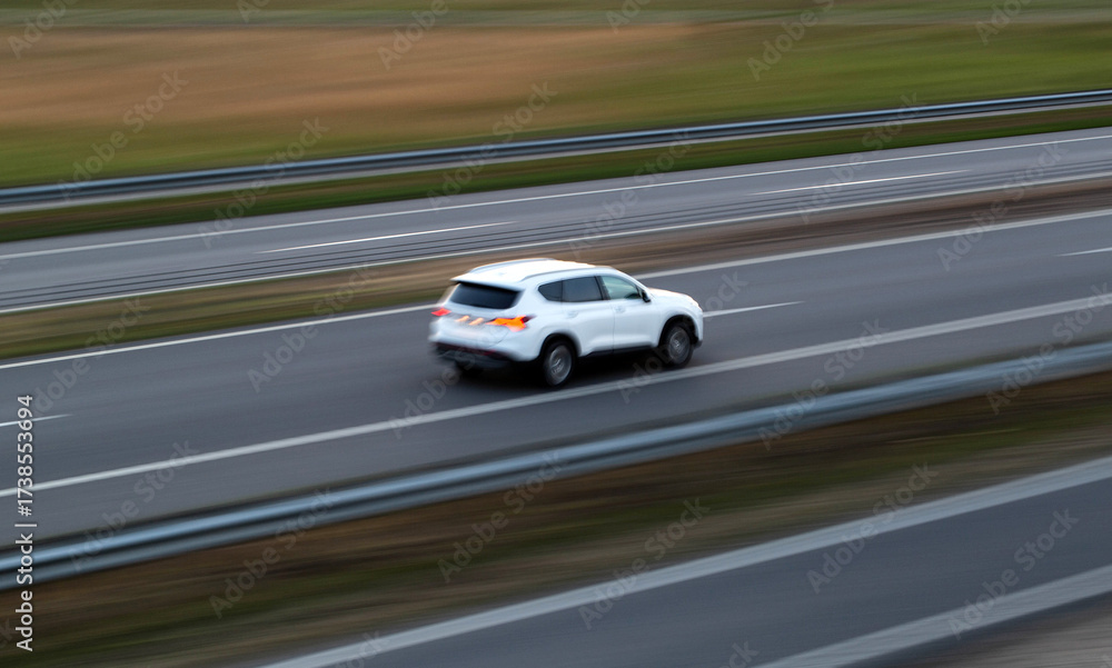 Fototapeta premium Fast-moving white SUV on a highway during early evening with blurred background