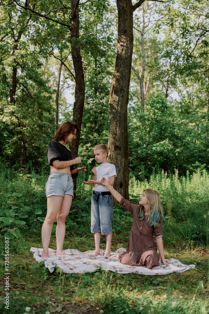 Obraz premium A young mother joyfully plays with her daughter and son in nature, sharing authentic family moments of laughter and connection. Pure love and outdoor happiness