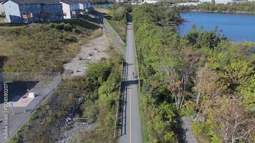 Wallpaper Mural Drone Captures Speed And Determination As One Athlete Pedals Through A Scenic Nature Park In Nova Scotia, With Lush Green Trees And Crystal-Clear Lake In View, Embodying Pure Summer Fitness Spirit. Torontodigital.ca