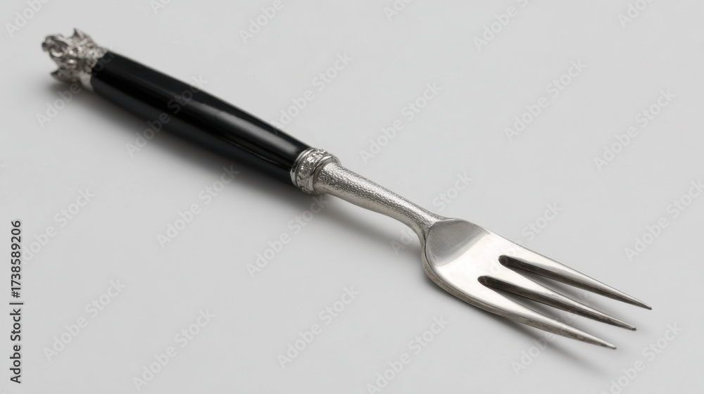 Fototapeta premium Elegant silver fork with a black enamel handle and gothic bat-inspired detailing on light gray background