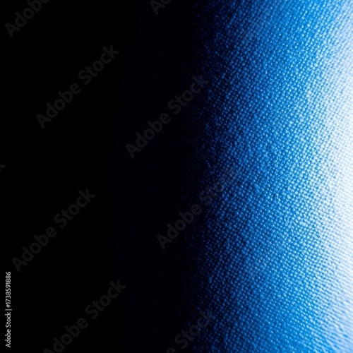 Close-up abstract texture of a dark blue fabric with a bright light illuminating the right side, creating a gradient effect.