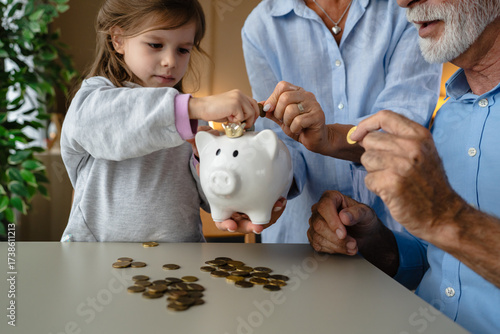 Bild auf Leinwand Grandparents teaching grandchild saving money in piggy bank