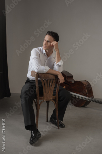 young man sitting on a chair near contrabass and thinking