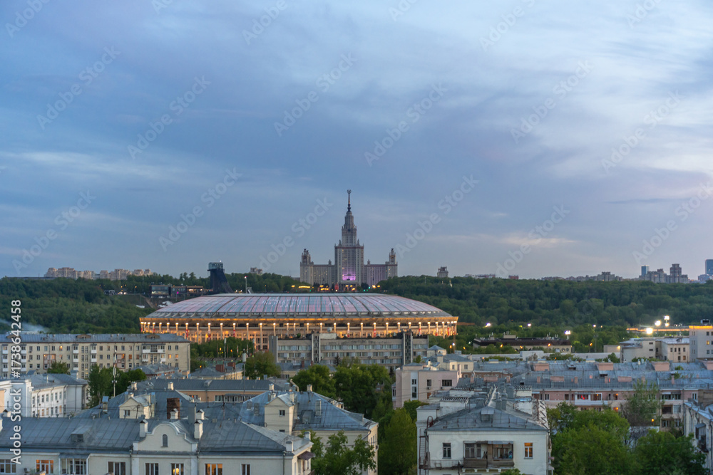 Naklejka premium A stunning scene captures a large sports stadium and an iconic building in Moscow as the sky transitions into twilight, creating a beautiful backdrop against city architecture.