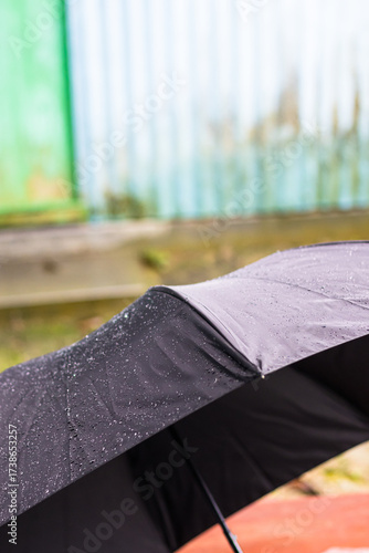 Wet Black Umbrella in Rain, Artistic Outdoor Closeup with Green and Blue Wall