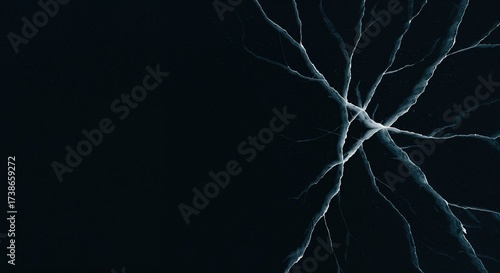 A dark, icy surface displays a complex network of bright, white and blue cracks radiating from a central point, creating an abstract pattern with ample copy space on the left side.