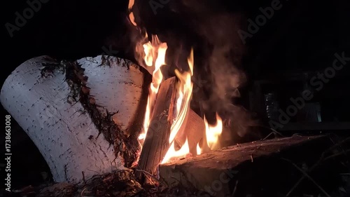 Tea in a transparent glass against the backdrop of a fire at night, with yellow leaves falling from the trees in late autumn
