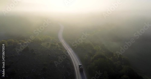Aerial view of truck driving on winding road through foggy forest