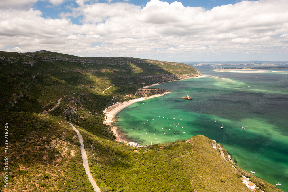 Fototapeta premium Scenic aerial shot of Praia de Alpertucho beach, located in beautiful Arrabida National Park, Portugal, surrounded by lush green hills and clear turquoise waters