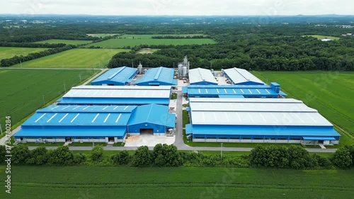 Aerial View of a Large Industrial Complex with Blue Roofs Surrounded by Green Fields