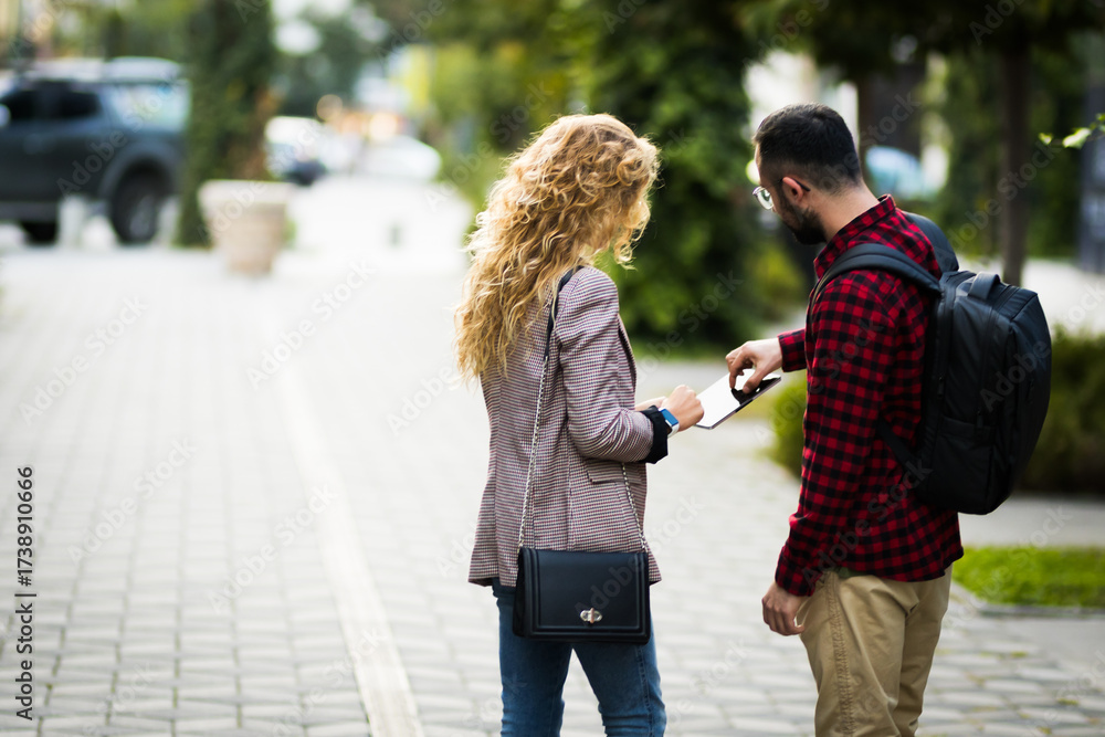 Obraz premium Young man and woman collaborating outdoors, utilizing modern technology in a natural setting. They are standing and engaging over a digital tablet, showcasing teamwork and communication on a pleasant