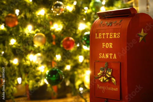 Christmas mailbox for mailing letters to Santa Claus. Closeup. Defocused Christmas tree with lights and ornaments in the background.