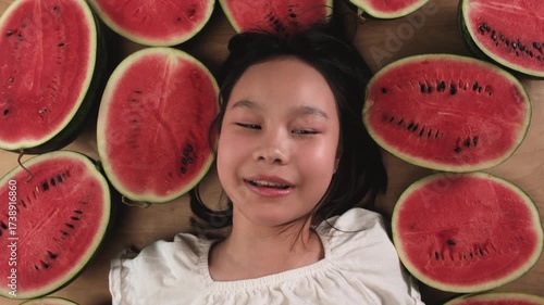 Portrait of a happy, cheerful Asian young girl with many half pieces of fresh red watermelons, fun enjoyment, a smile, and looking at camera in healthy eating and abundant fruit, happiness summertime.