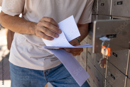 A young man reads a letter while standing at a mailbox.