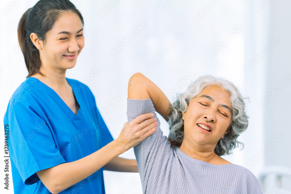 Fototapeta premium Young nurse trains elderly woman to exercise her arm during therapy and rehabilitation in her living room at home. Physical therapist.