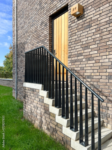 brick house exterior with wooden door, staircase and black metal railing