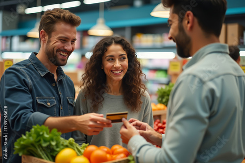 Couple paying with credit card at supermarket checkout. Shoppers using card to pay for groceries. Happy people making cashless payment.