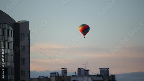 Colorful hot air balloon soaring above the rooftop of residential building in St. Petersburg city at sanset, Russia
