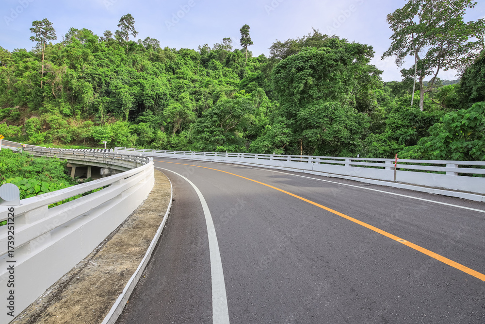 Fototapeta premium Road with a white railing on the side and trees in the background