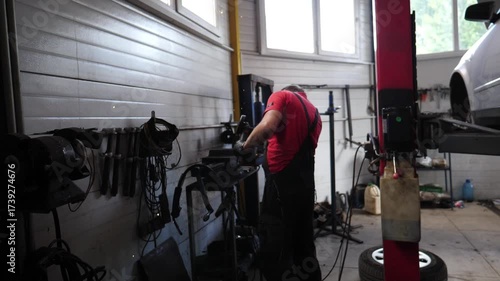 Skilled automotive technician in red shirt engaged in car repair, sparks flying from grinding tool, showcasing dynamic action and craftsmanship in a busy garage environment