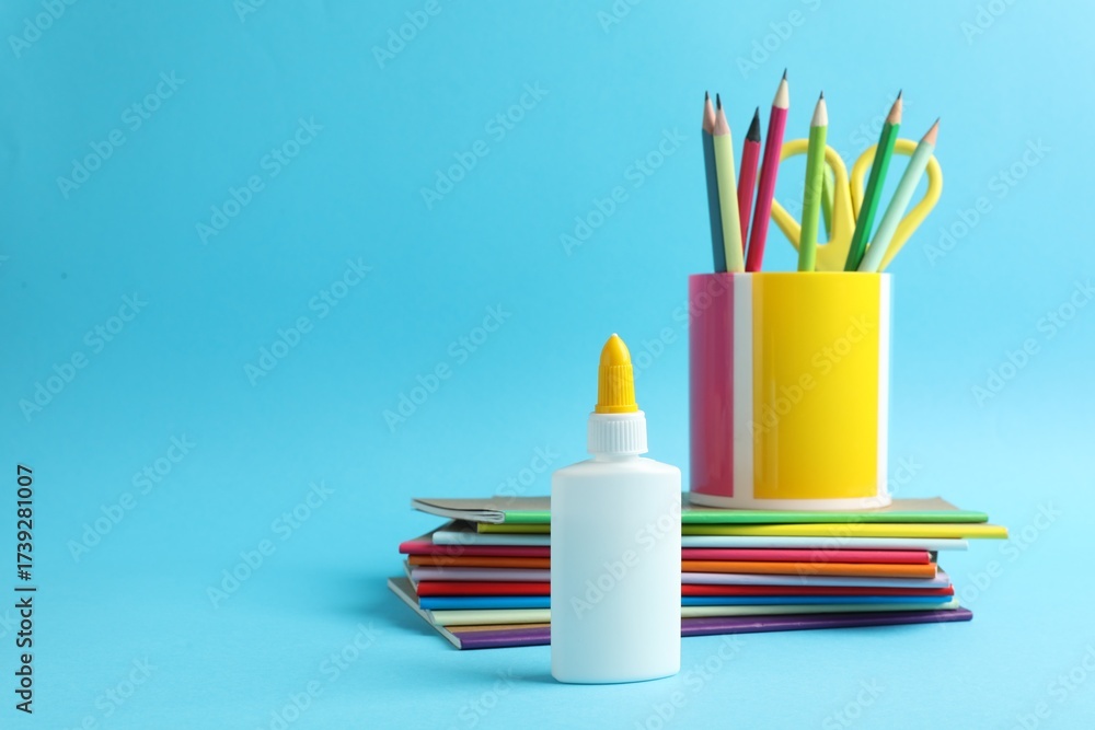 Obraz premium Glue in bottle, notebooks, color pencils and scissors on light blue background, closeup. Space for text