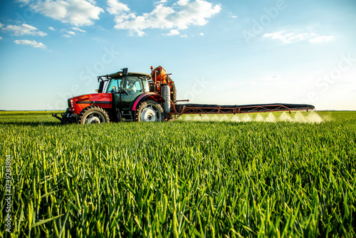 Farm tractor spraying green wheat crop field with pesticide