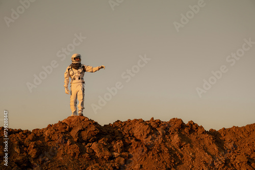 Astronaut in spacesuit exploring alien terrain and stretching hand toward the horizon.
