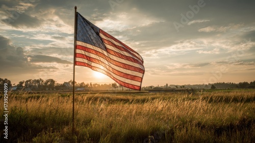 Sunset casts warm glow over American flag waving in open field surrounded by nature and soft clouds
