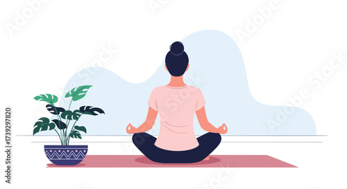 A person sits in a meditative pose on a yoga mat near a potted plant.