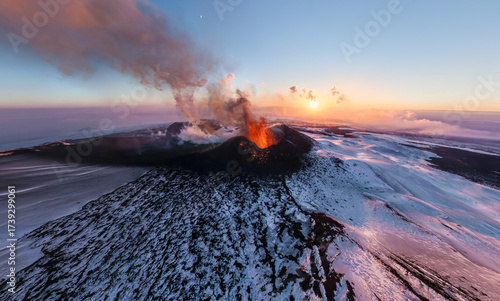 Aerial view of a volcanic eruption with fiery orange lava contrasting against the snowy landscape under a pastel sky, Klyuchi settlement, Kamchatka Krai, Russia.