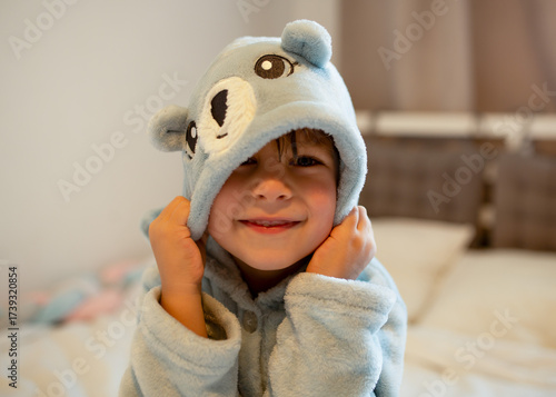 Принти на полотні Cute child in a soft blue bathrobe with bear ears smiling after bath time, sitting on the bed