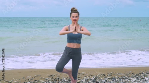 A girl meditates standing on the beach in the morning. A woman does morning meditation in a standing pose on the seashore in super slow motion.