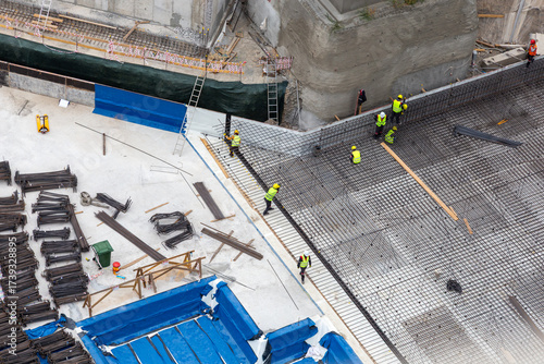 Construction Workers Cooperate On Reinforcement Grid Across Foundation At Busy Site
