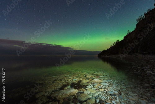 Fototapeta Naklejka Na Ścianę i Meble -  Stunning nightscape of the green aurora borealis and stars reflecting on the calm, clear waters of the Baltic Sea coast, Paldiski, Estonia.