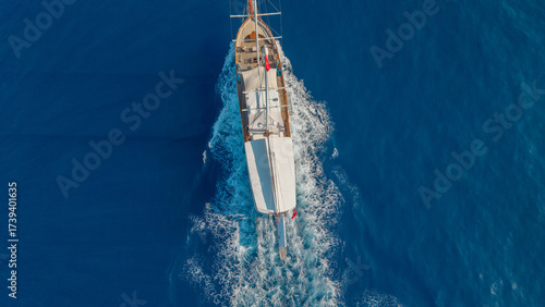 Foto Sailing Vessel on the Blue Sea: A traditional wooden sailing vessel gracefully glides across the tranquil expanse of the azure sea