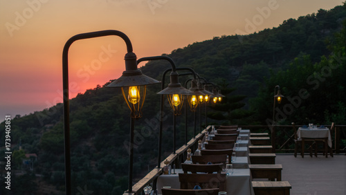 Bild auf Leinwand Outdoor Restaurant View at Sunset: A captivating restaurant, featuring lamps, overlooks the serene embrace of a sunset