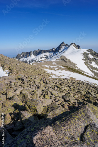 Snowy peaks and rocky terrain of Sierra de Gredos, Spain, beneath a vivid blue sky. The dramatic mountain landscape highlights rugged summits and pristine alpine environment.