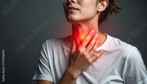 Young woman suffering from sore throat pain touching her neck. Female holding hand on red highlighted inflamed throat area feeling discomfort ache. Person experiencing health issue problem.