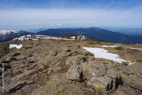 High-altitude view from Peñalara Summit (Sierra de Guadarrama), Spain. Rocky and lichen-covered terrain with patches of snow overlooking distant mountain ranges and valley.