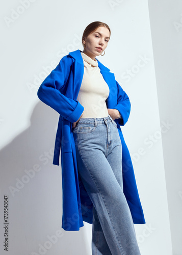 a beautiful woman in a long blue coat on a light background