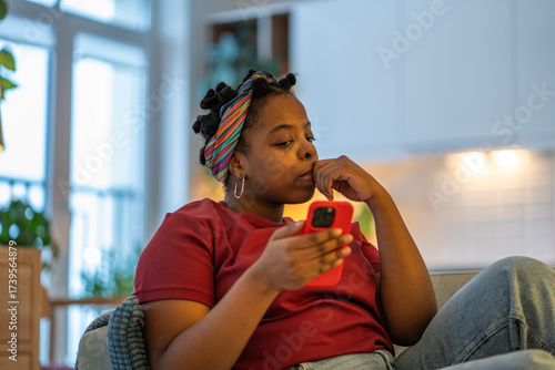 Fotografi Anxious millenial woman sits on couch at home with phone feels nervous while reading online news or personal message