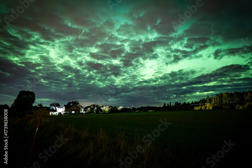 Northern lights dancing behinde the dark cloud over country landscape