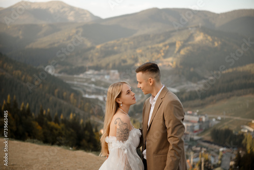A beautiful, happy young couple in love on a wedding walk and photo shoot high in the mountains. The groom in a jacket and suit and the bride in a white dress at a resort. Kissing and hugging