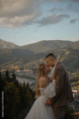 A beautiful, happy young couple in love on a wedding walk and photo shoot high in the mountains. The groom in a jacket and suit and the bride in a white dress at a resort. Kissing and hugging
