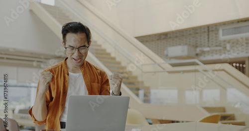 Senior Asian businessman wearing headset celebrates success during online meeting in modern co-working space. Remote work and business communication concept	