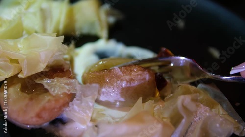 Fork breaking caramelized pear with crispy puff pastry and creamy syrup on black plate by woman hand close up elegant gourmet dessert restaurant presentation.