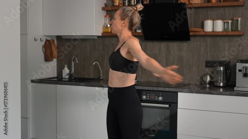 Woman in dark sportswear exercising at home with kitchen background. Home workout in small apartment.