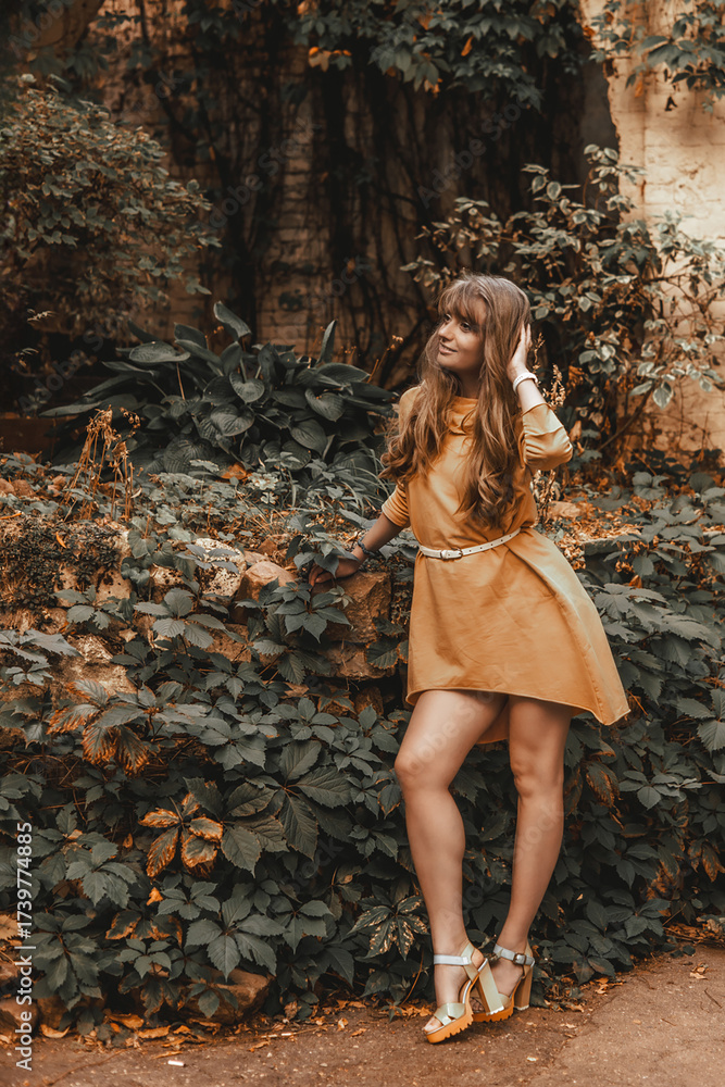 Naklejka premium Portrait of a blonde woman in a yellow dress on the city streets. Autumn