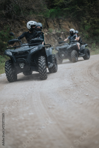 Fényképezés A group of friends enjoy an outdoor adventure, riding all-terrain quad bikes on a dusty dirt road surrounded by nature and trees, sharing a thrilling and memorable experience together
